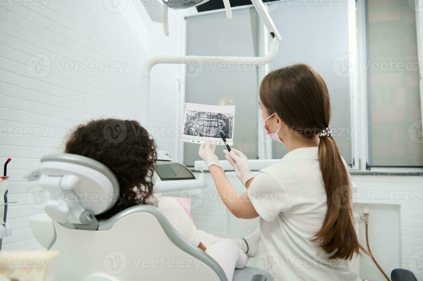 Rückseite Aussicht von ein weiblich Zahnarzt Hygieniker zeigen geduldig ein Panorama- Röntgen von Kiefer und Zähne während ein medizinisch Untersuchung im ein modern Dental Klinik. das Konzept von medizinisch Diagnose im Zahnheilkunde foto