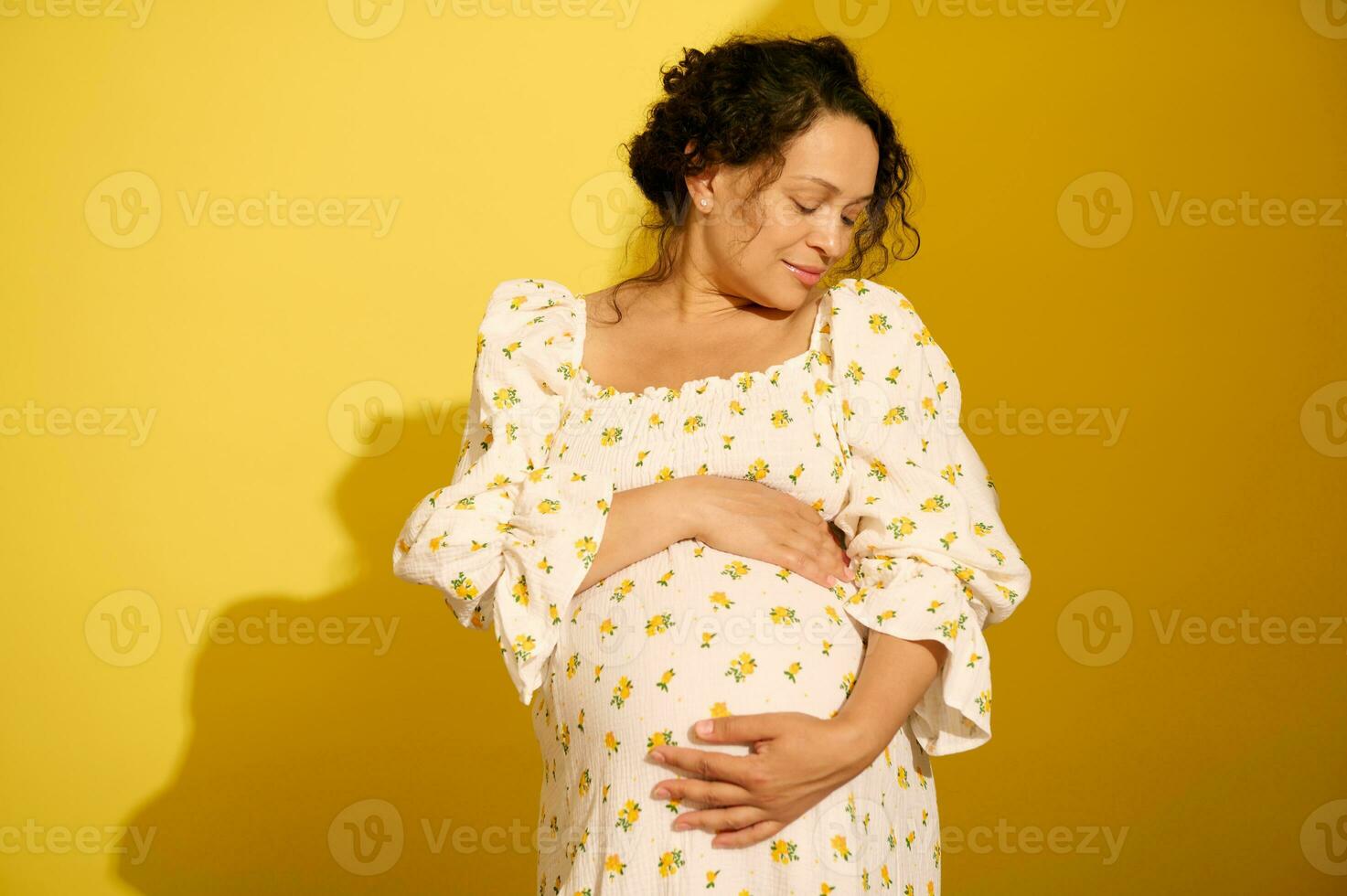 glücklich gravid schwanger Frau sanft streicheln und umarmen ihr groß Bauch, isoliert Über Gelb Studio Hintergrund foto