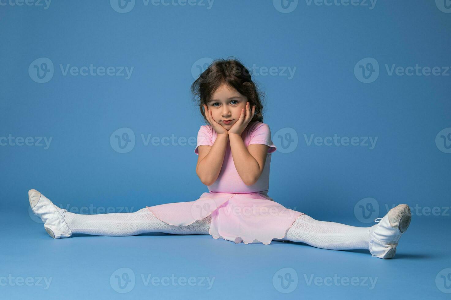 süß Ballerina im Rosa Kleid perfektionieren Schnur während Sitzung auf Blau Hintergrund foto