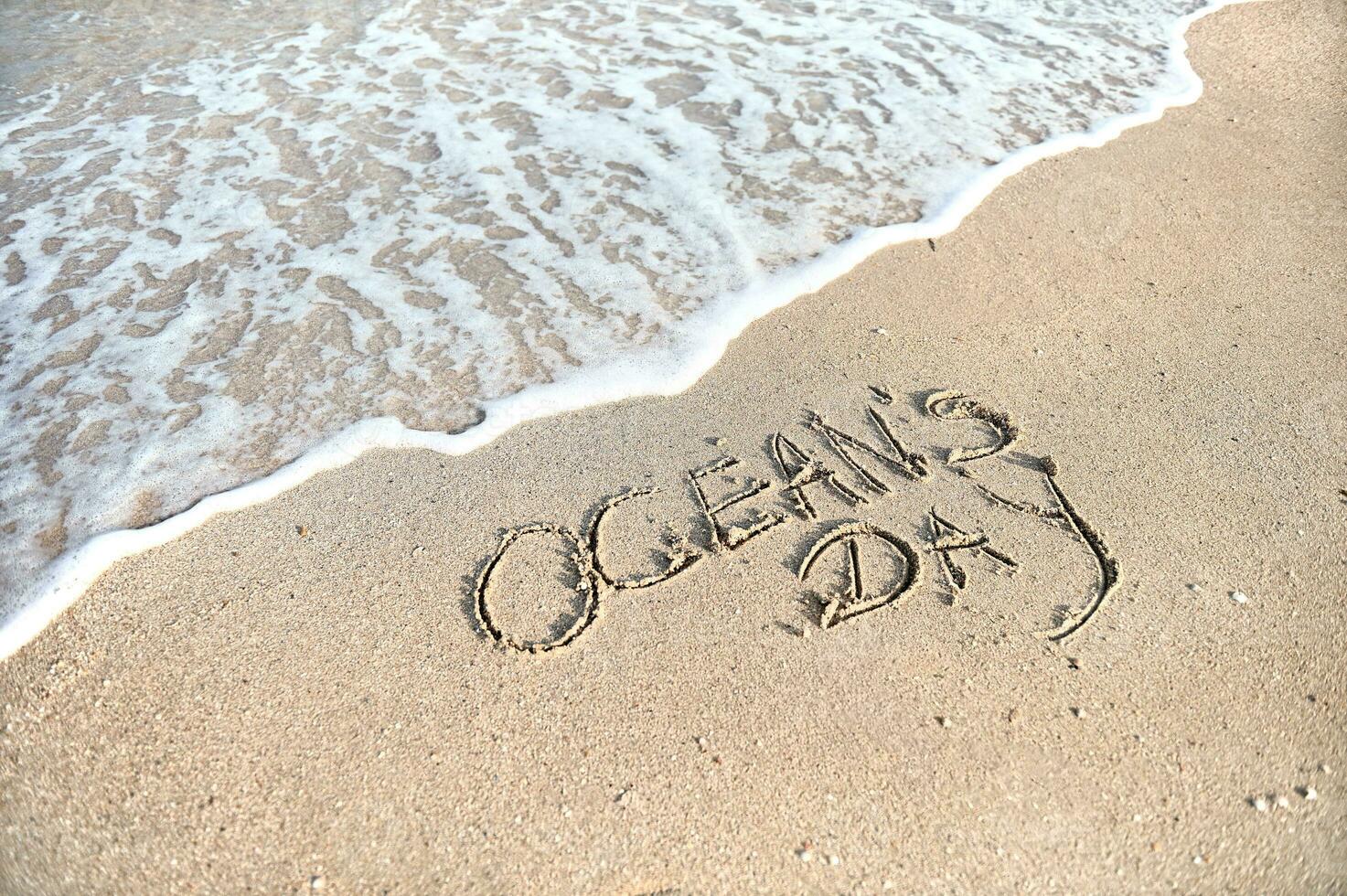 Inschrift des Ozeans Tag auf golden Sand durch das Meer. Sommer- Konzept foto