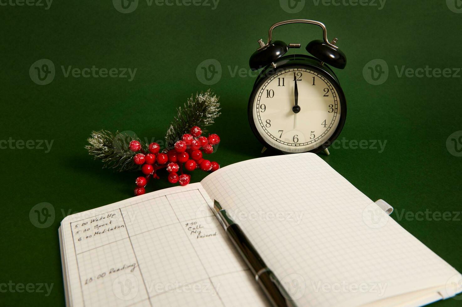 Nahansicht von ein geöffnet Seite von Notizblock mit Pläne zum Tag, Alarm Uhr und schneebedeckt Ast von Stechpalme Weihnachten Pflanze isoliert auf Grün Hintergrund foto