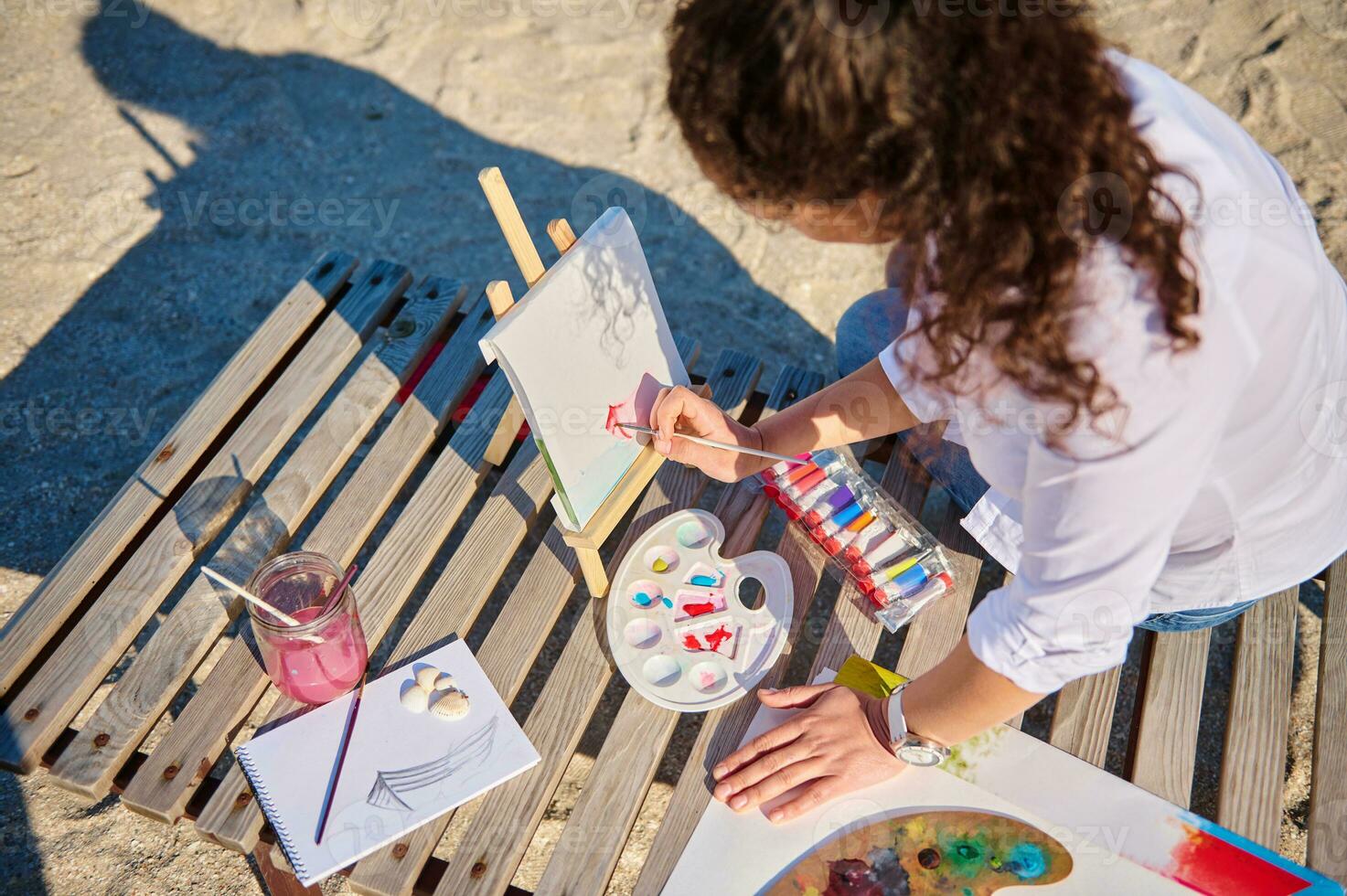 hoch Winkel Aussicht von ein weiblich Maler mit Aquarell Technik zu Farbe ein Bild im öffnen Luft auf das Strand foto