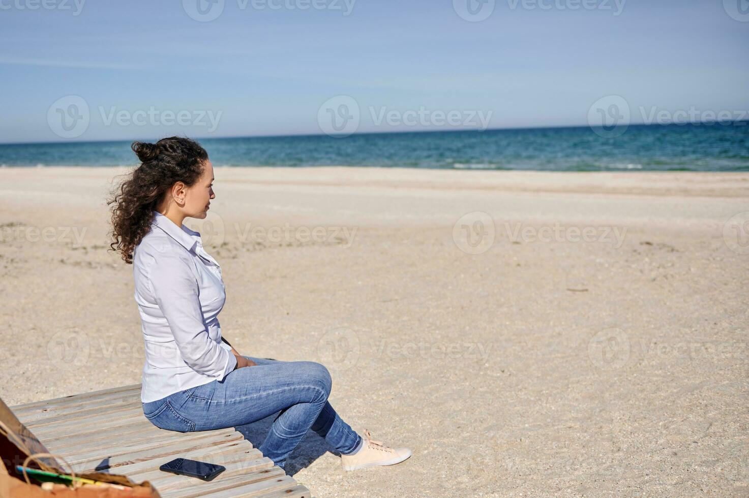 heiter Frau Sitzung auf ein hölzern Chaise Salon Sitzung auf einsam Strand und genießen das still Aussicht zu das Strand. still nicht städtisch Szene, Freizeit Aktivität und Entspannung Zeit Konzepte foto