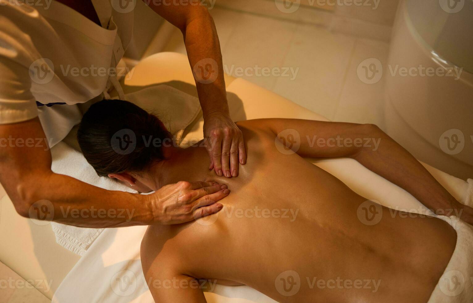 ayurvedisch Behandlung, Fachmann therapeutisch Körper Massage beim das Wellness Spa Klinik. Nahansicht von ein jung Frau entspannt sich während Lügen auf ein Massage Tabelle während ein therapeutisch zurück Massage beim Luxus Spa. foto