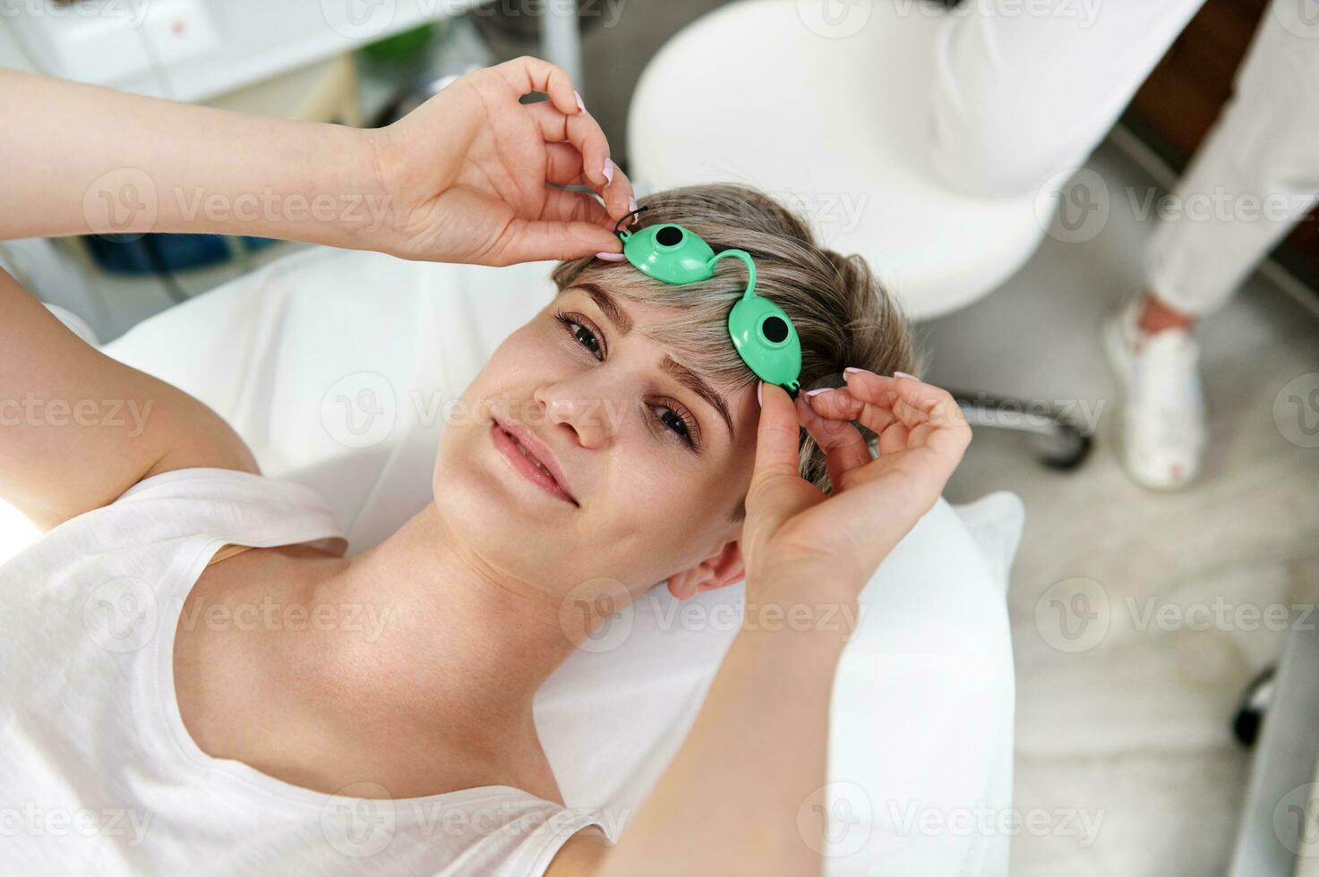 lächelnd schön Klient von Kosmetologie Klinik Putten aus schützend uv Brille nach Laser- Epilation Verfahren foto
