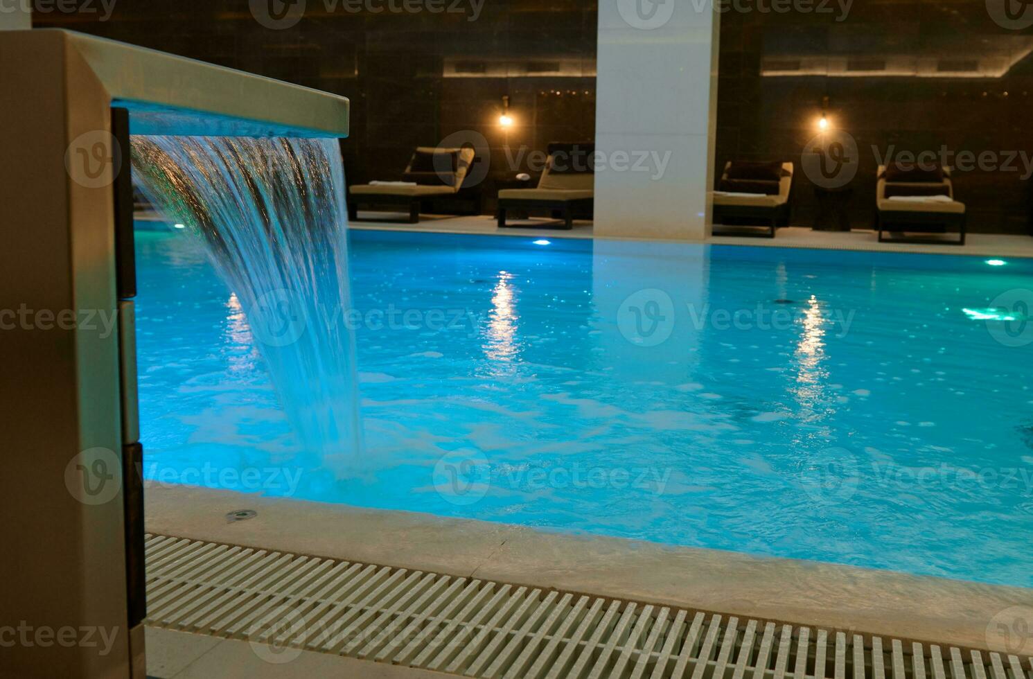 Innen- Thermal- Schwimmen Schwimmbad mit Wasserfall und unter Wasser Beleuchtungen im ein Luxus Salon Bereich von ein Wellness Spa Center foto