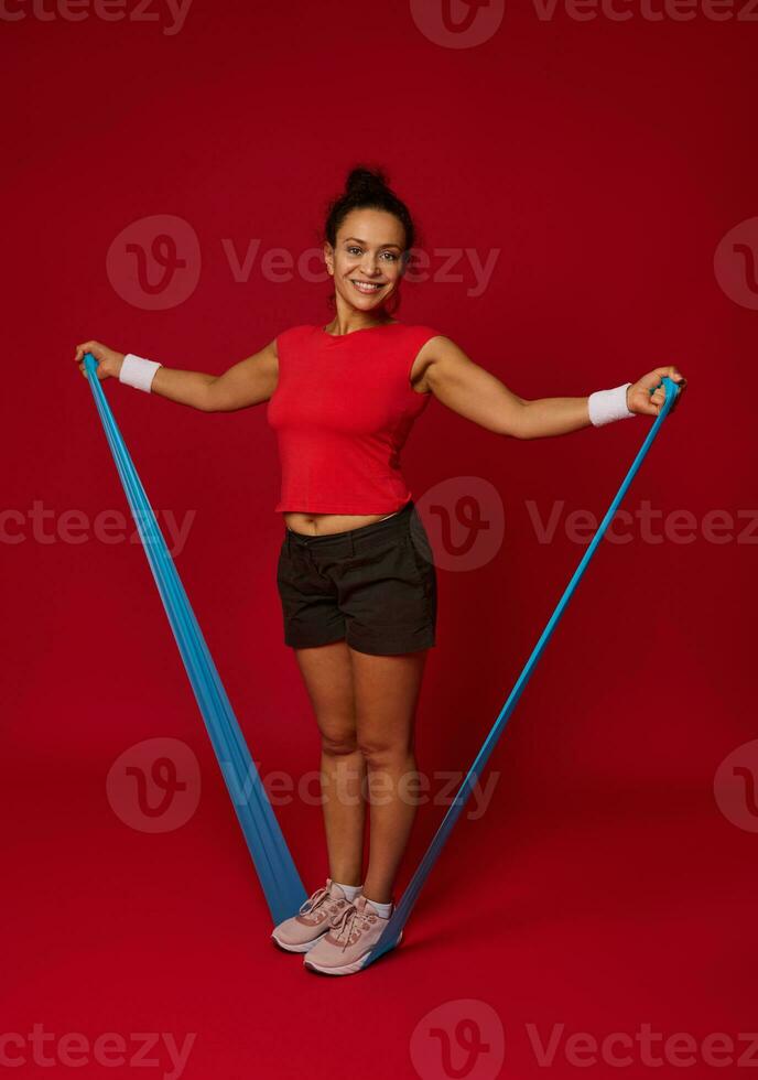 voll Länge von ein sportlich Frau mit Übung Band gegen rot Hintergrund mit Kopieren Raum zum Werbung Text. Fitness, Sport, aktiv und gesund Lebensstil Konzept foto