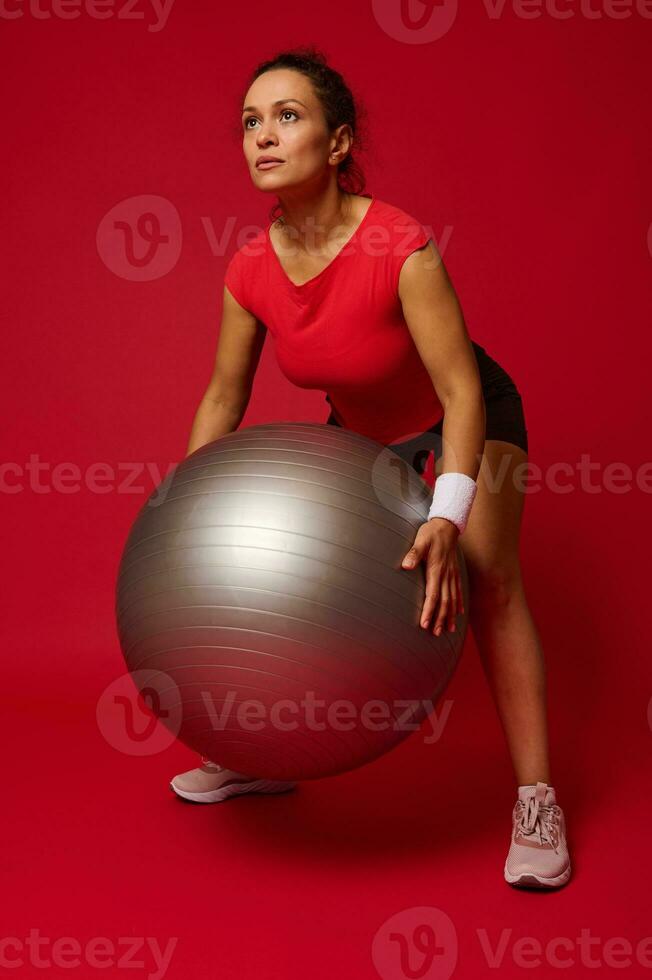 Mitte alt afrikanisch amerikanisch sportlich Frau, weiblich Athlet ausüben mit Fitness Ball gegen rot Hintergrund mit Kopieren Anzeige Raum zum Werbung Text foto