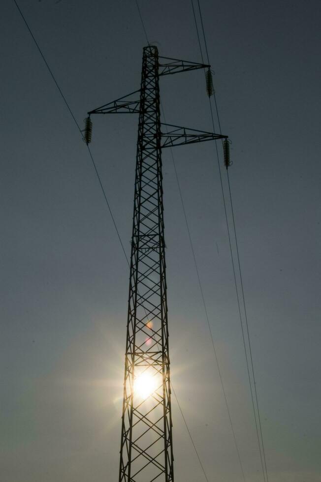 ein Silhouette von ein Elektrizität Turm mit das Sonne hinter es foto