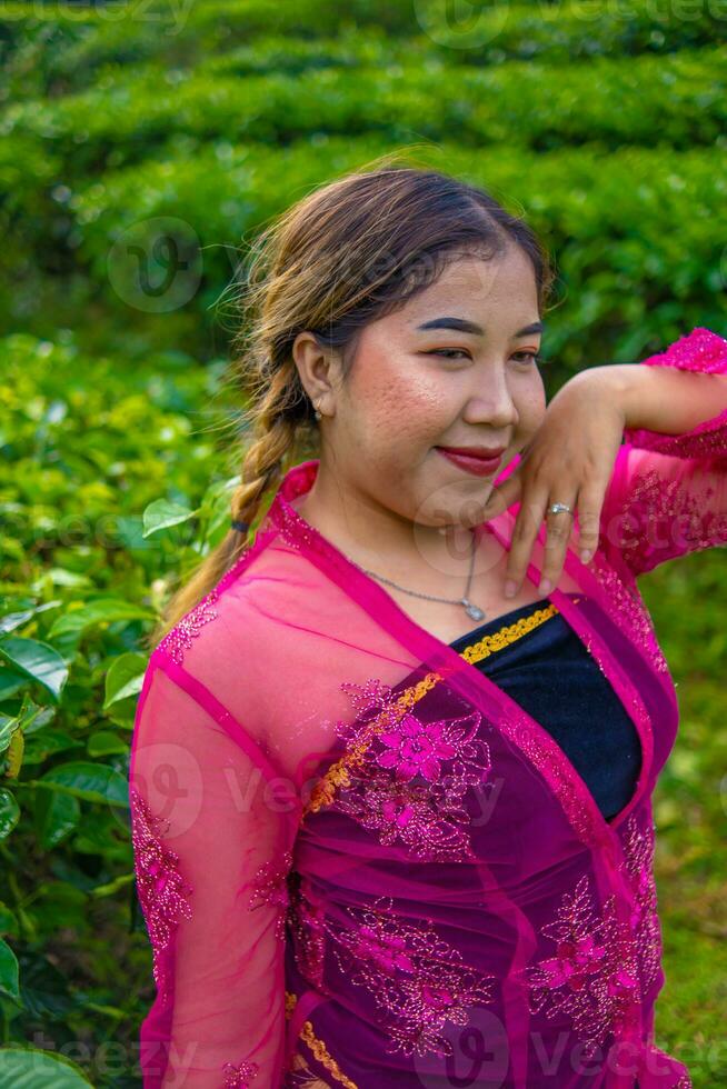 ein asiatisch Frau im ein traditionell Rosa Kostüm ist Stehen sehr elegant im ein Tee Plantage foto