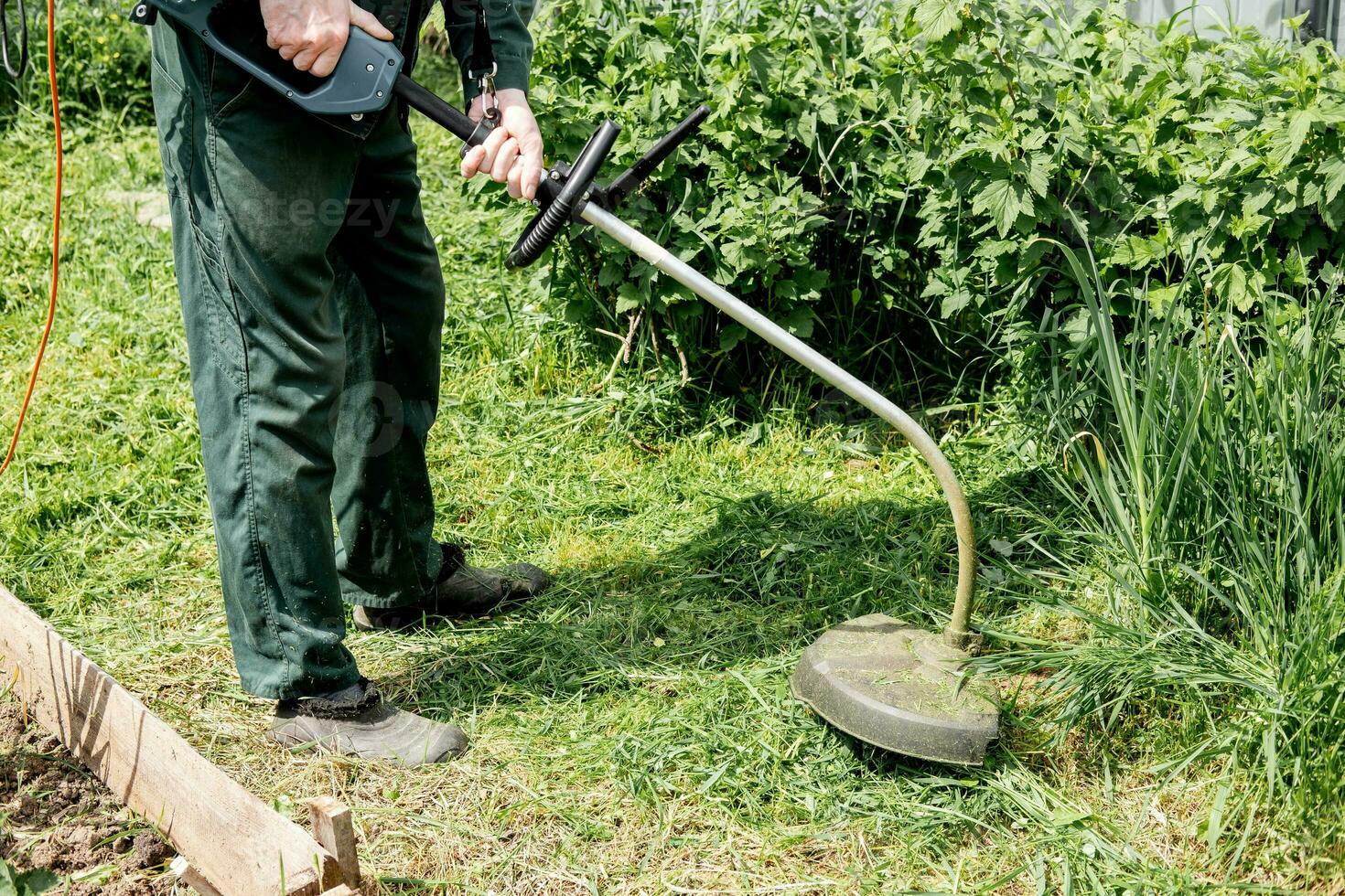 Mann mäht Rasen Gras mit ein Rasen Mäher. Benzin Rasen Mäher, Trimmer Nahansicht. Mann Arbeiten im das Garten foto