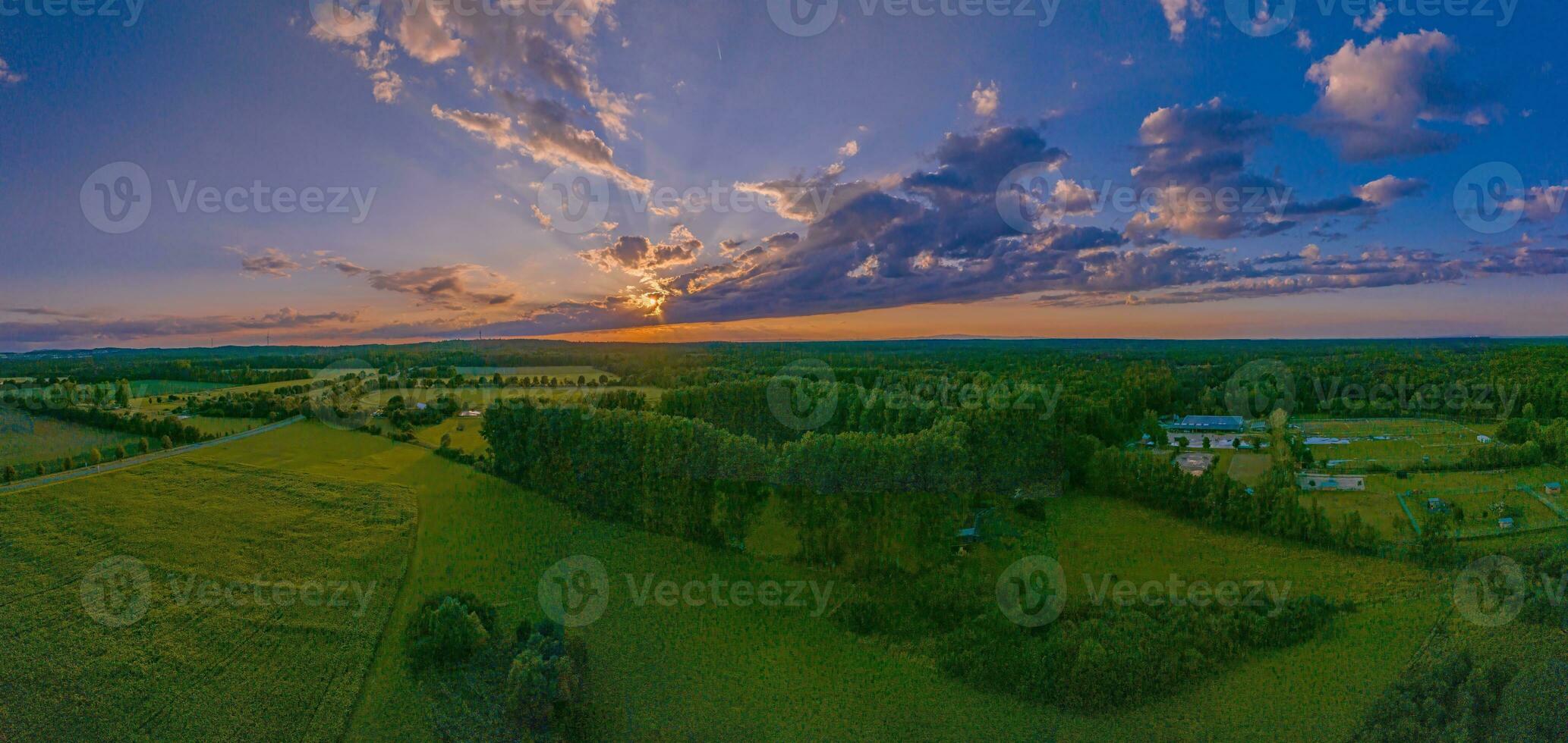 Drohne Panorama von ein Sonnenuntergang hinter Wolken mit Sonne Strahlen Über Wiesen und Felder foto