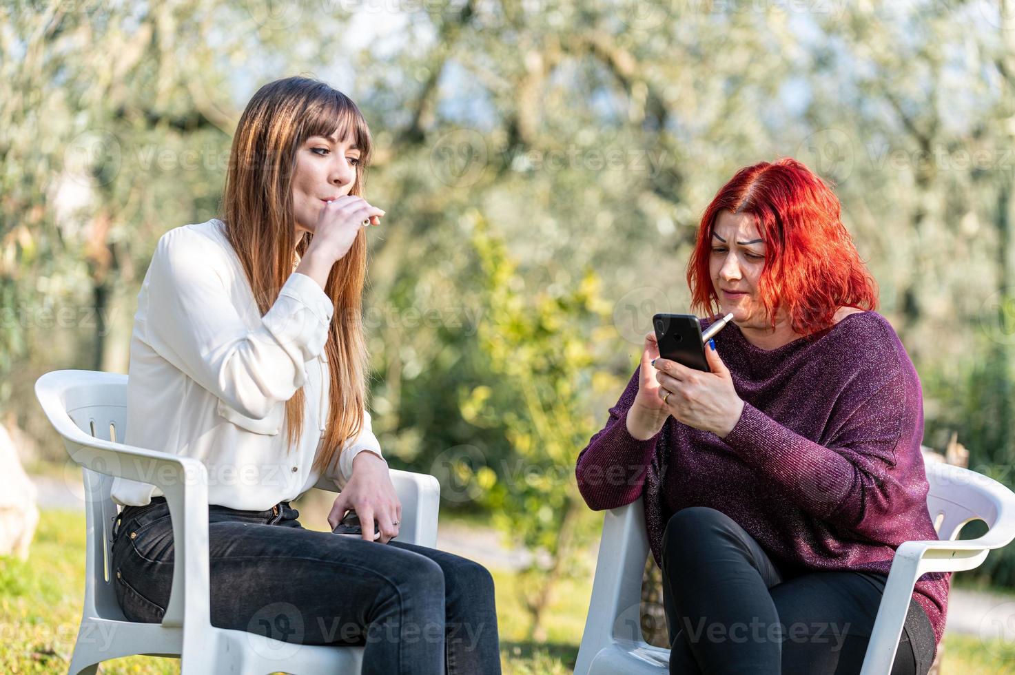 Freundinnen mit Smartphone und Zigarette rauchen foto