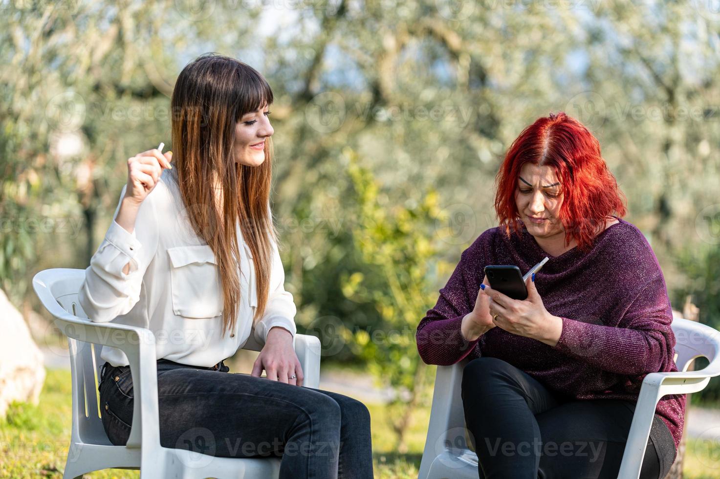 Freundinnen mit Smartphone und Zigarette rauchen foto