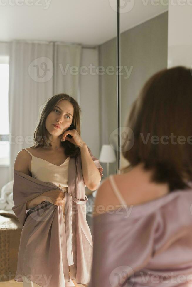 glücklich Morgen. attraktiv jung Frau suchen im Spiegel beim ihr Wohnung foto