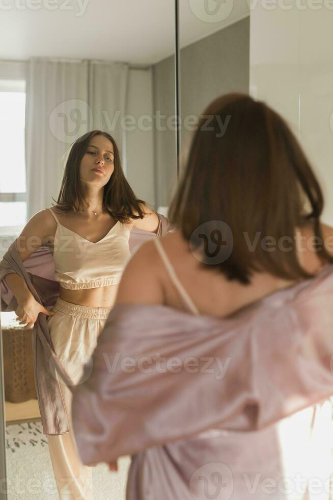 glücklich Morgen. attraktiv jung Frau suchen im Spiegel beim ihr Wohnung foto