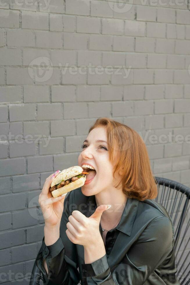 ein jung Frau isst ein Burger mit Fleisch auf ein Sommer- Terrasse foto