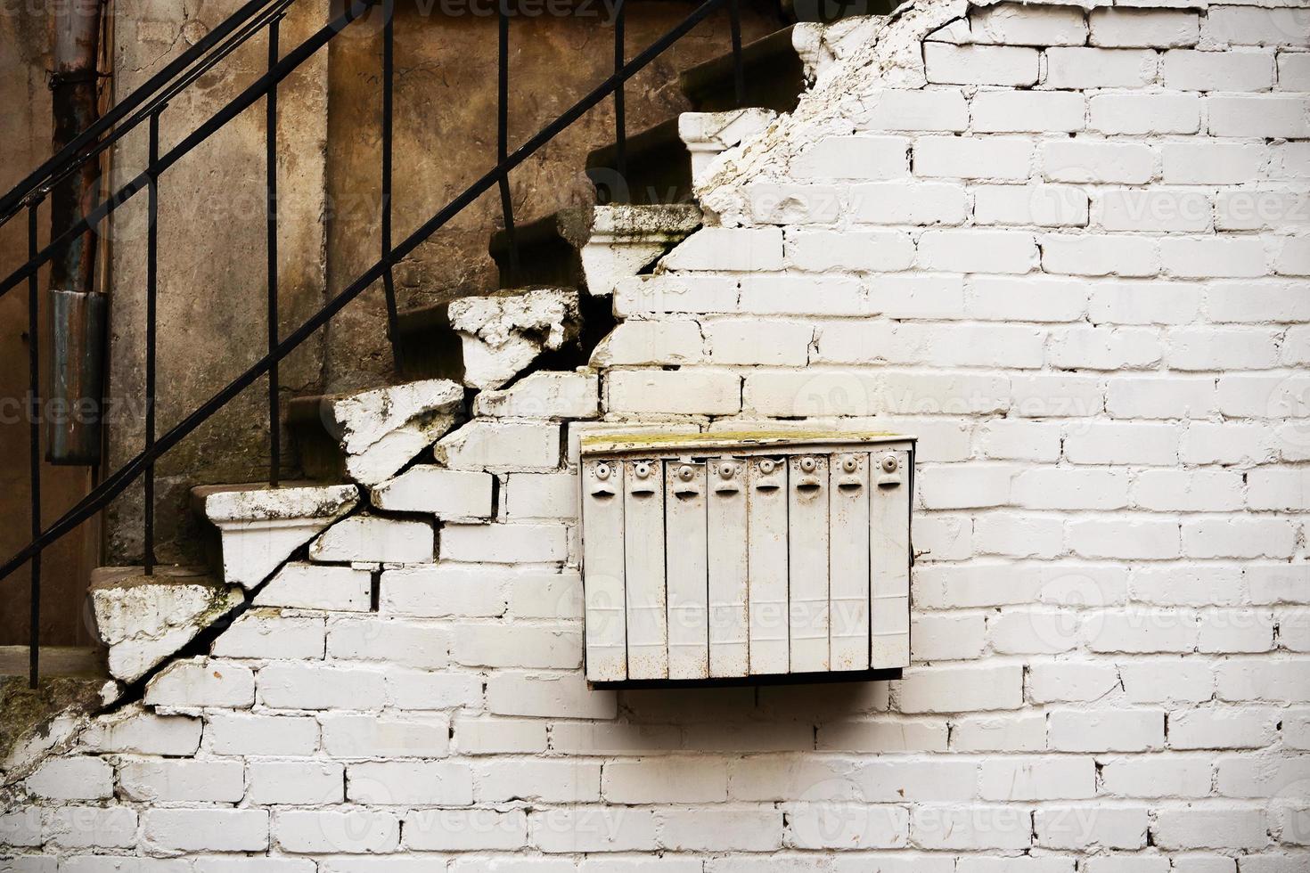 weißer Briefkasten mit mehreren Abteilungen, der an einer weißen Mauer unter der Treppe hängt foto