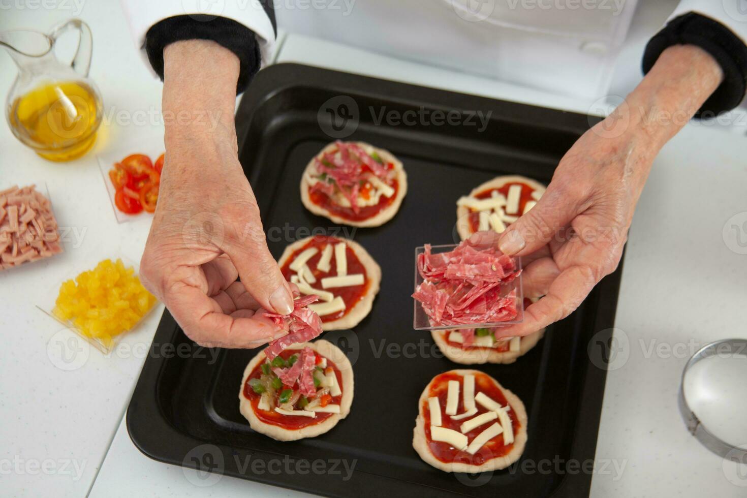 Hinzufügen Belag zu das Mini Pizzen. Hinzufügen Salami. köstlich hausgemacht Mini Pizza Vorbereitung. foto