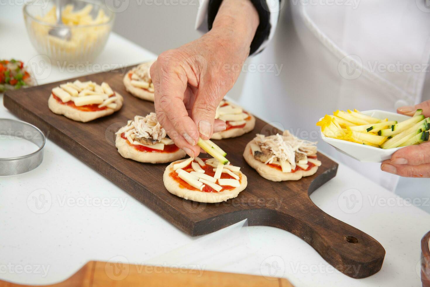 Hinzufügen Belag zu das Mini Pizzen. Hinzufügen Gemüse. köstlich hausgemacht Mini Pizza Vorbereitung. foto