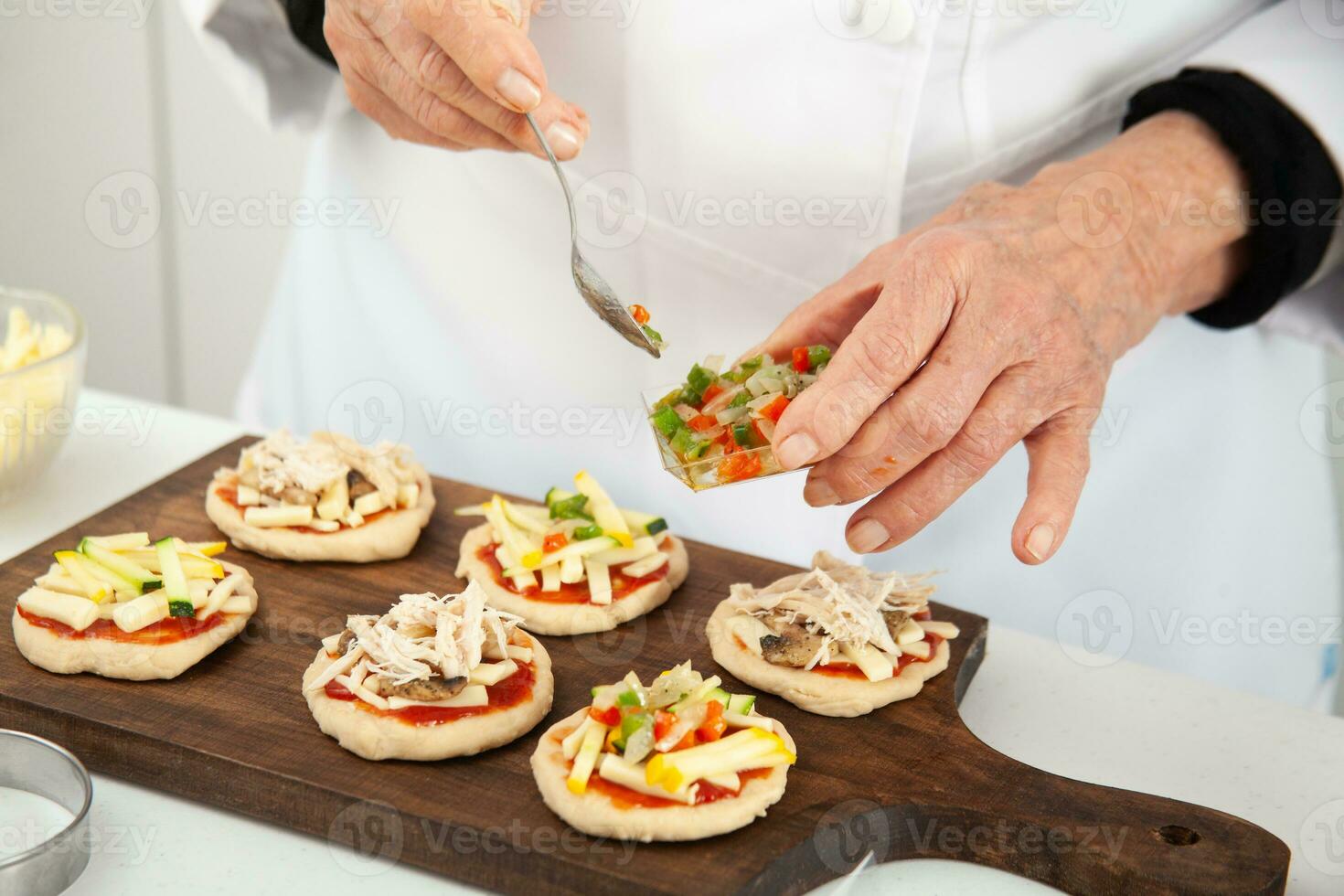 Hinzufügen Belag zu das Mini Pizzen. Hinzufügen Gemüse. köstlich hausgemacht Mini Pizza Vorbereitung. foto