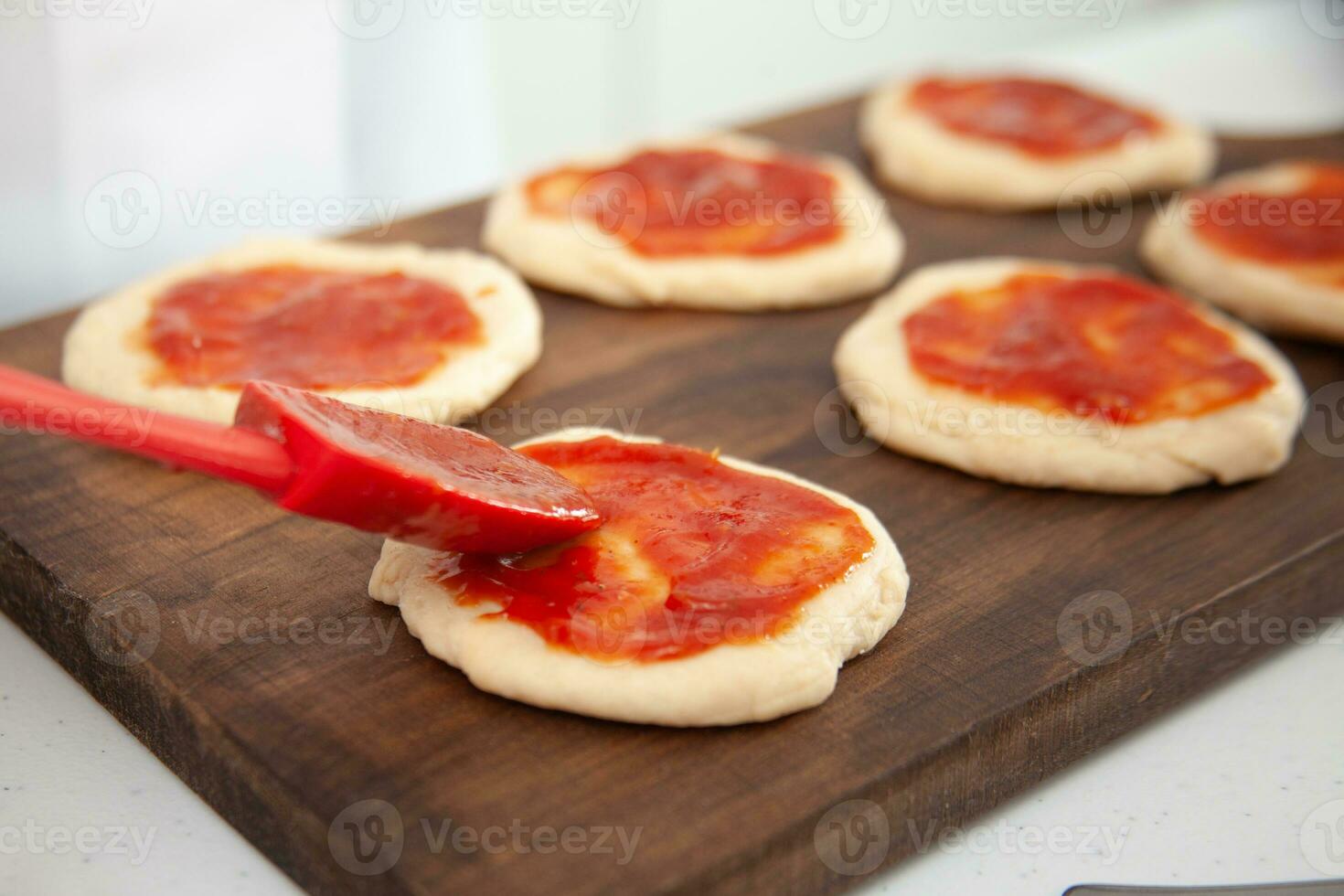 Senior Frau Hinzufügen Pizza Soße zu das gedehnt Teig. köstlich hausgemacht Mini Pizza Vorbereitung. foto