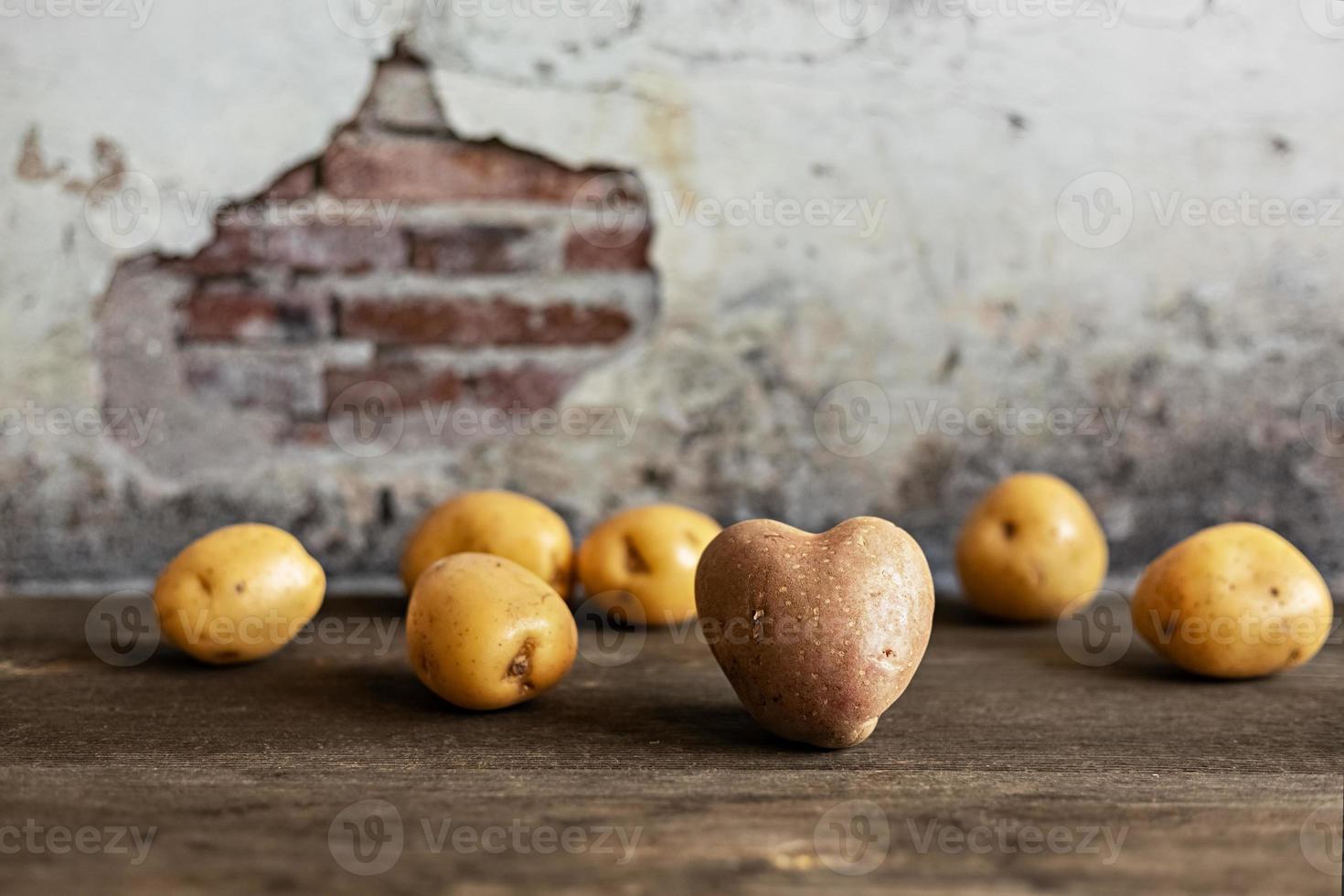 Herzförmige rote Kartoffel unter weißen Kartoffeln auf Vintage-Hintergrund foto