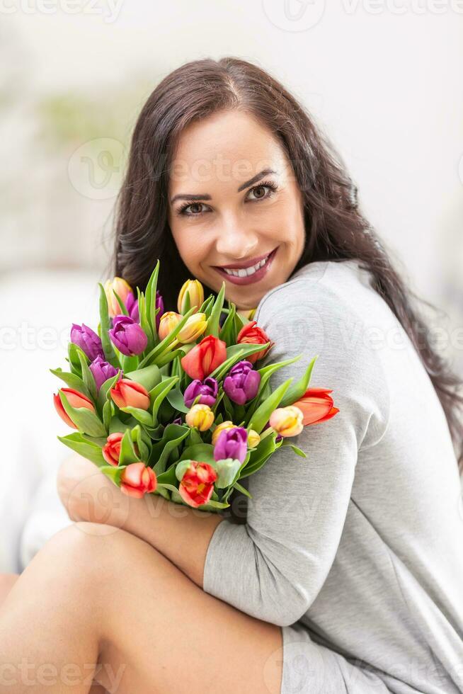 glücklich dunkel behaart Frau halten ein schön Strauß voll von Tulpen während National Damen Tag foto