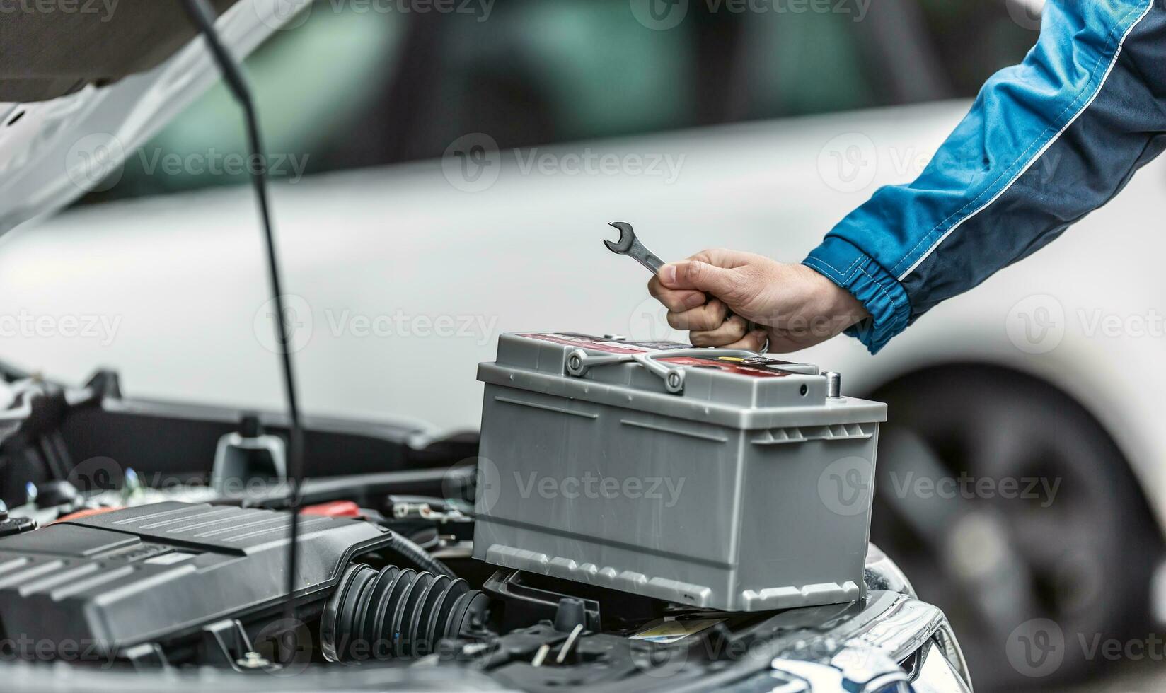 Mechaniker hält Schlüssel Über Auto Batterie mit Motor Kofferraum von das Auto öffnen foto