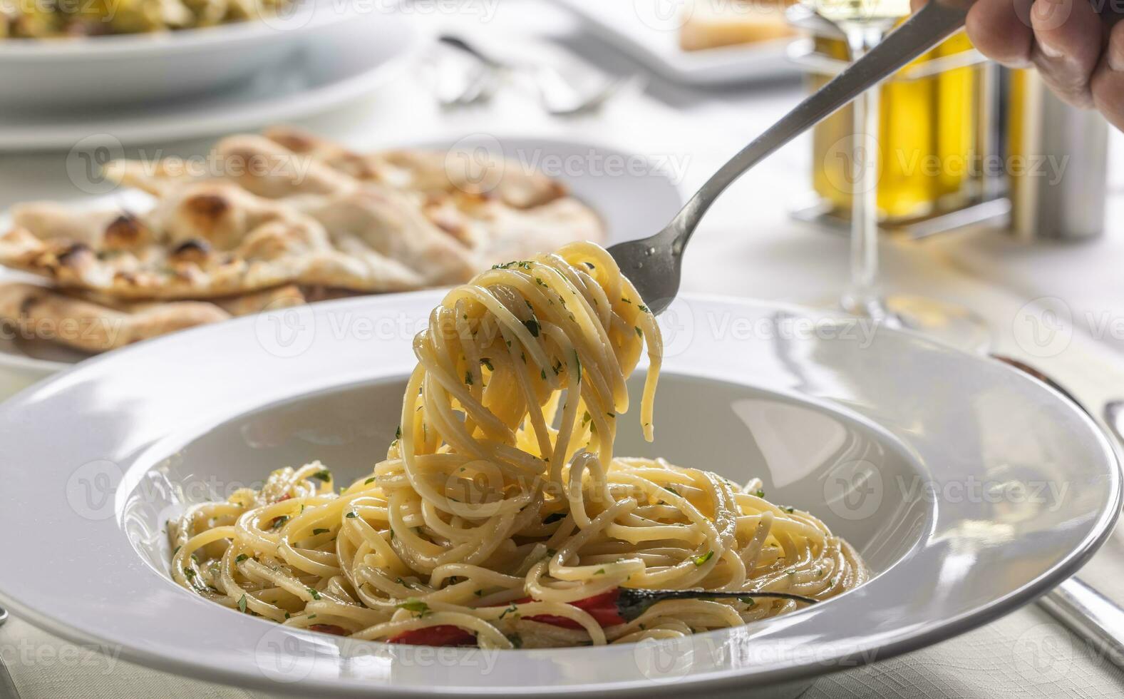 Hand mit ein Gabel Spinnen Spaghetti Aglio e olio peperoncino von ein Teller im ein Restaurant foto