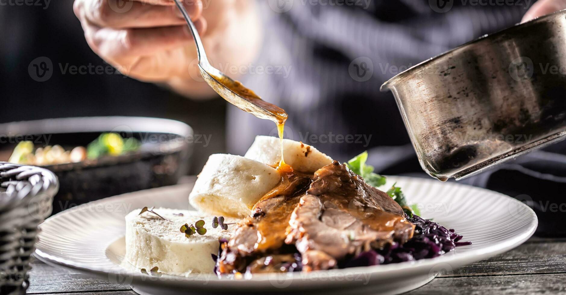 Essen dekorieren Hand von ein Koch gießt Soße Über herzhaft Essen von Fleisch, Knödel und Kohl foto