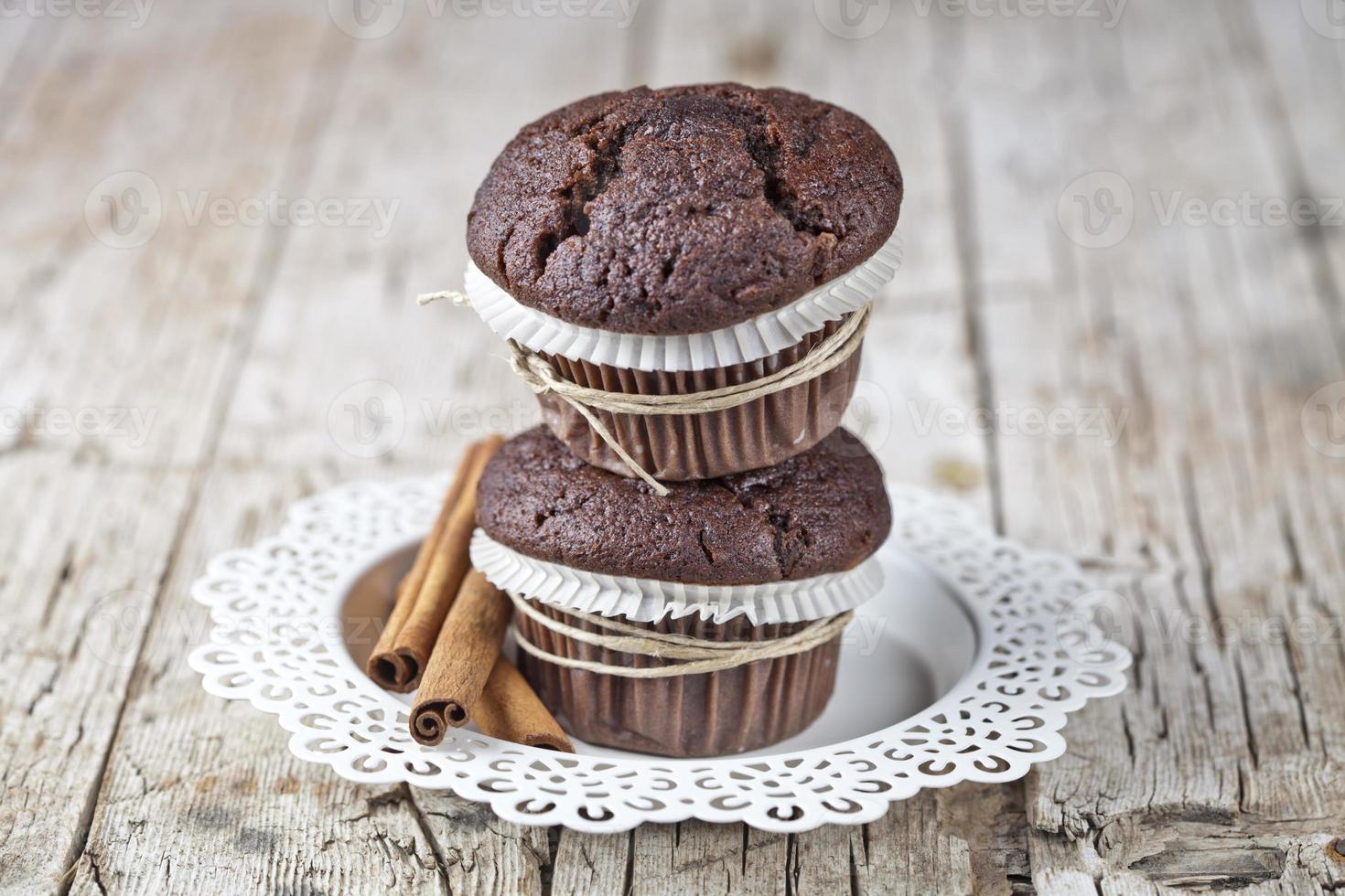 Frische dunkle Schokoladenmuffins mit Zimtstangen auf weißem Teller auf rustikalem Holztisch. foto