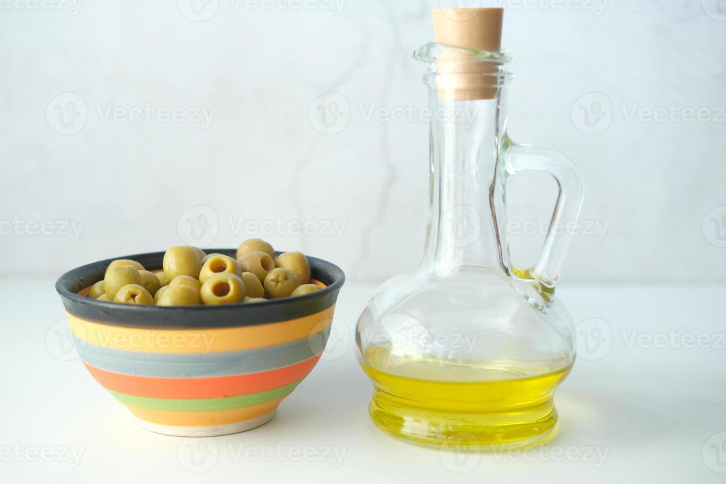 Flasche Olivenöl und frische Oliven in einem Behälter auf dem Tisch foto