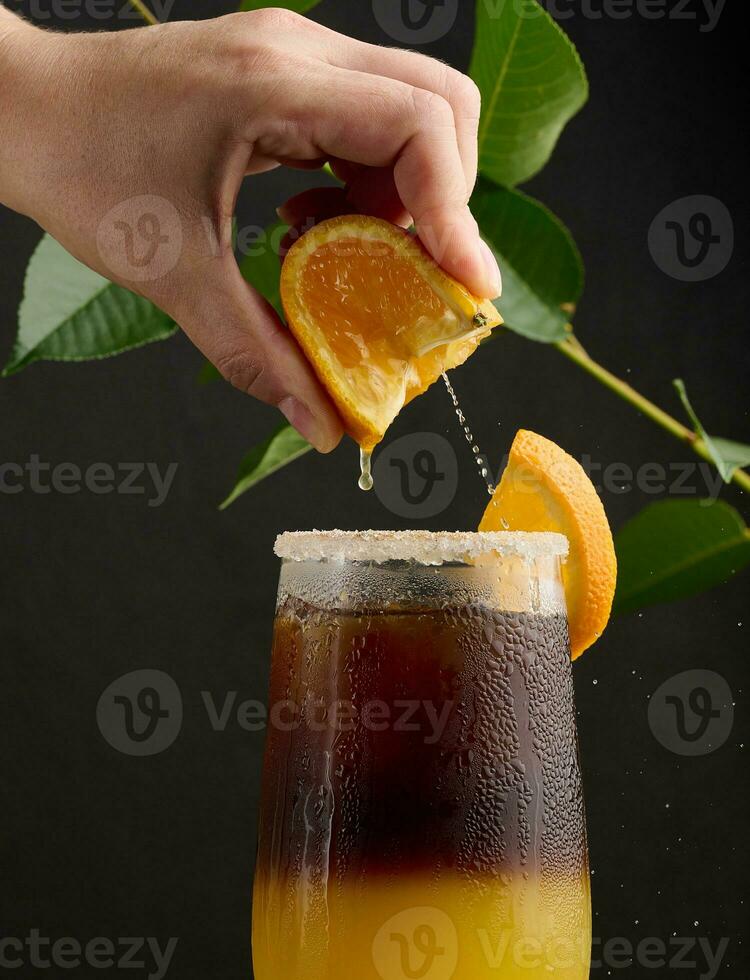 vereist Kaffee mit Orange Saft im ein transparent Glas, ein Frau Hand drückt ein Orange Scheibe in ein Blase trinken foto