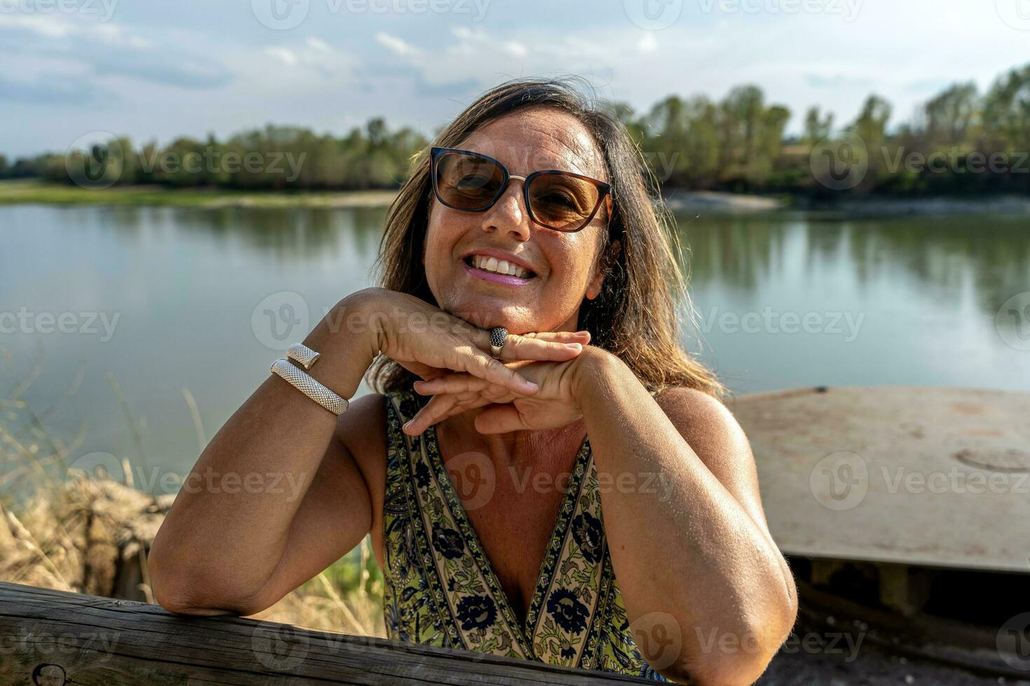 Porträt von schön Mitte alt Dame tragen Sonnenbrille auf das Banken von das Fluss foto