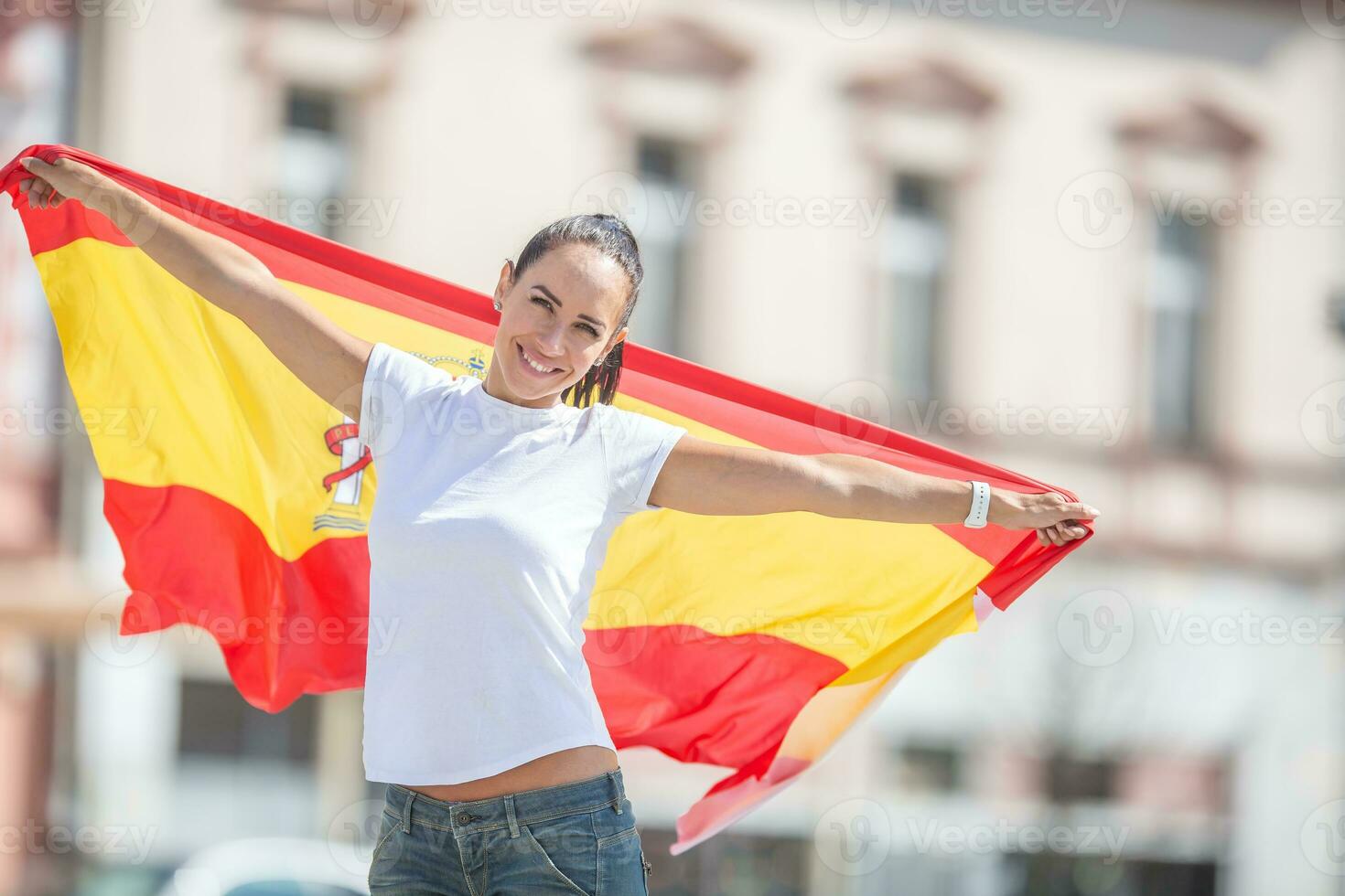 schön Mädchen hält ein Spanisch Flagge im ihr Hände hinter ihr, Jubel auf ein Straße foto