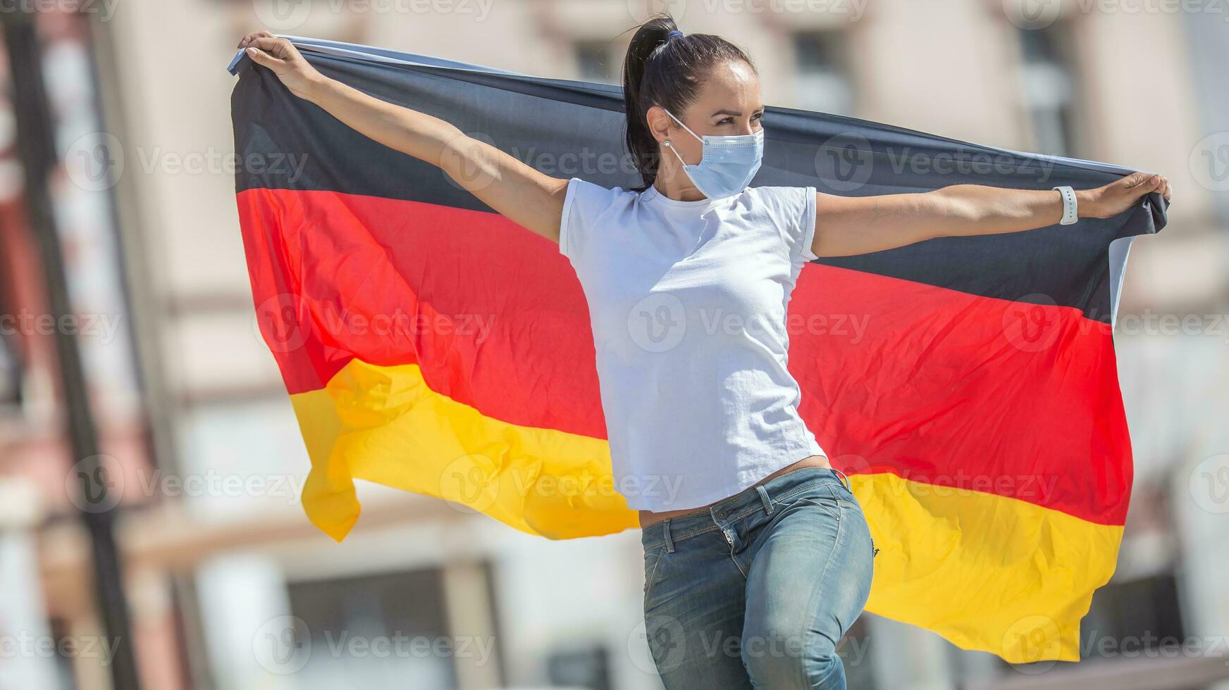 Frau tragen ein Gesicht Maske hält ein Flagge von Deutschland hinter ihr foto