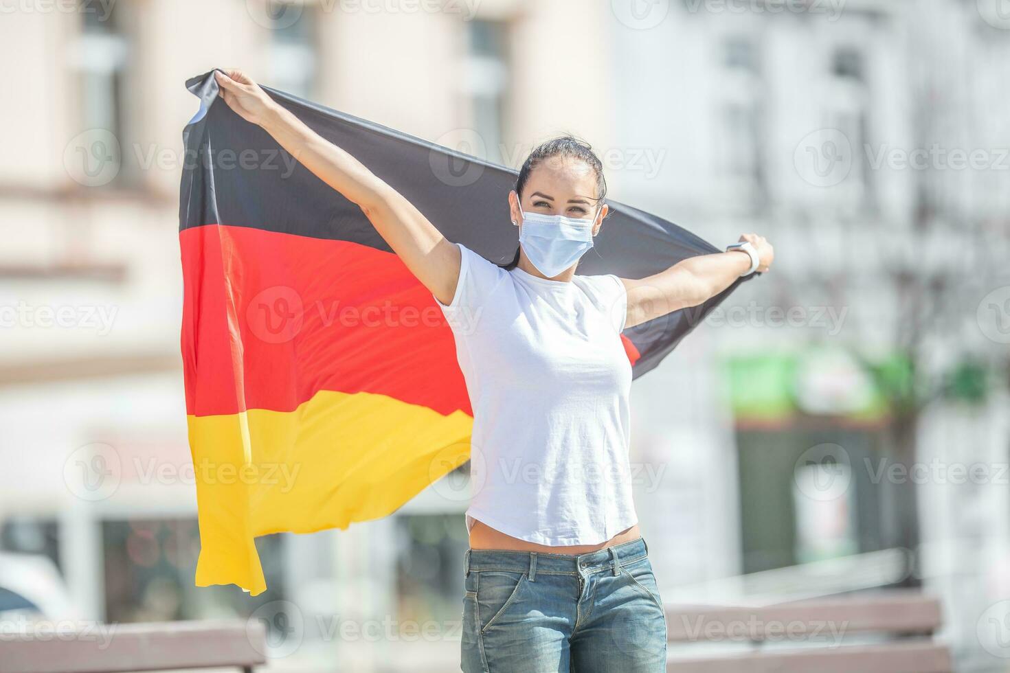 Deutsche Ventilator im ein Gesicht Maske hält das Flagge hinter ihr draußen, lächelnd foto