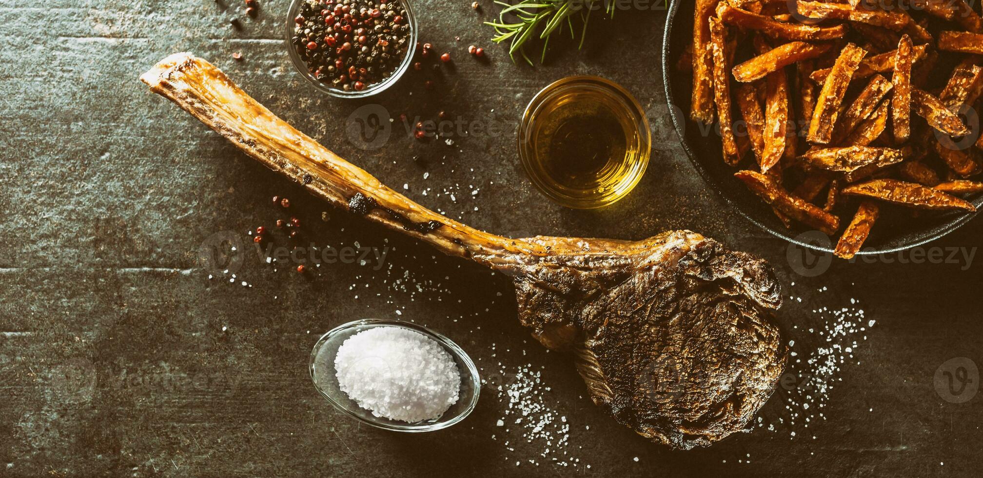 gegrillt Rindfleisch Tomahawk Steak mit Süss Kartoffel Fritten Salz- Gewürze Olive Öl und Rosmarin auf rustikal Tafel - - oben von Aussicht foto