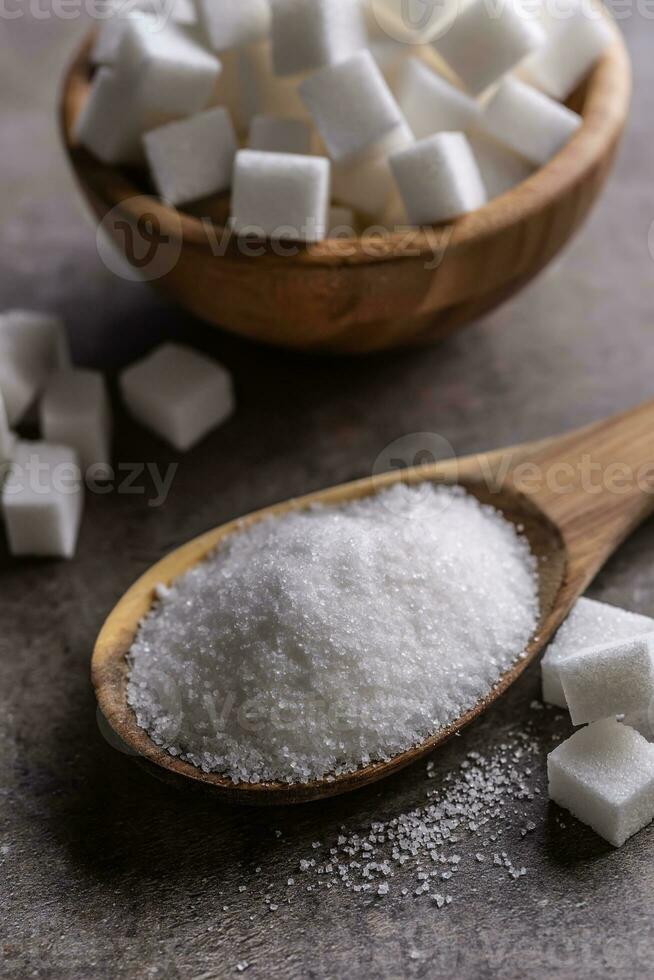 Weiß Kristall Zucker im ein hölzern Löffel und Würfel Zucker Nächster zu es foto