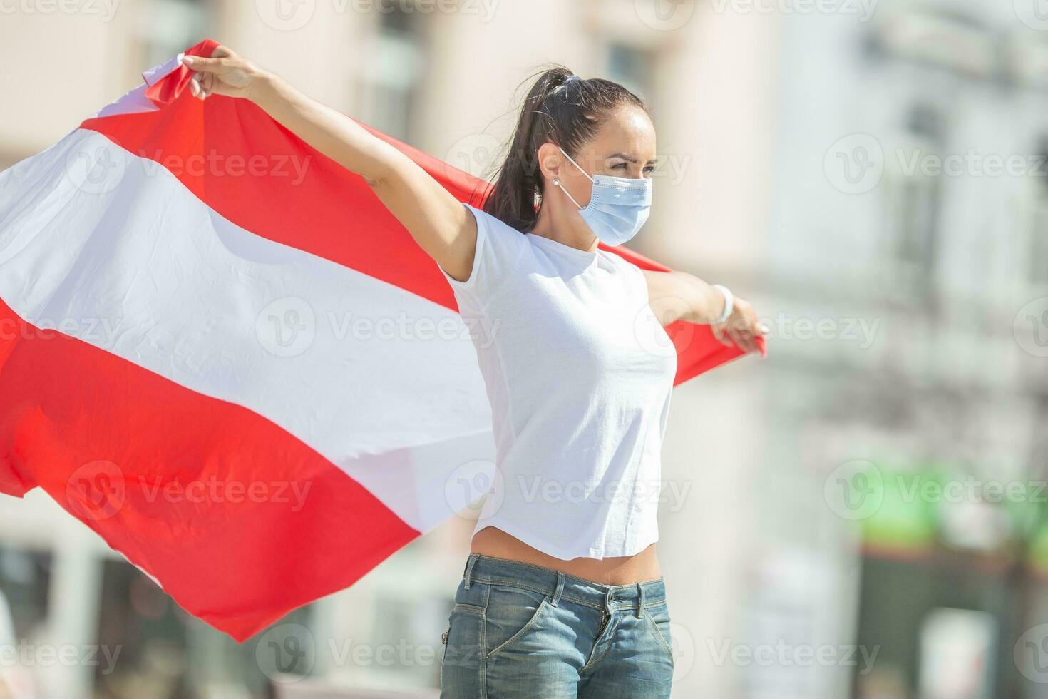 weiblich im schützend Maske hält ein Flagge von Österreich hinter ihr draußen auf ein sonnig Tag foto