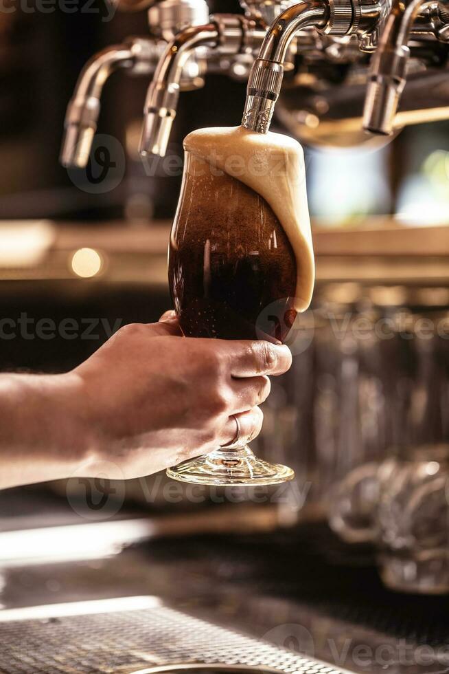 Schaum Gießen Nieder das Glas von ein frisch getippt dunkel Bier im ein Kneipe oder ein Restaurant foto