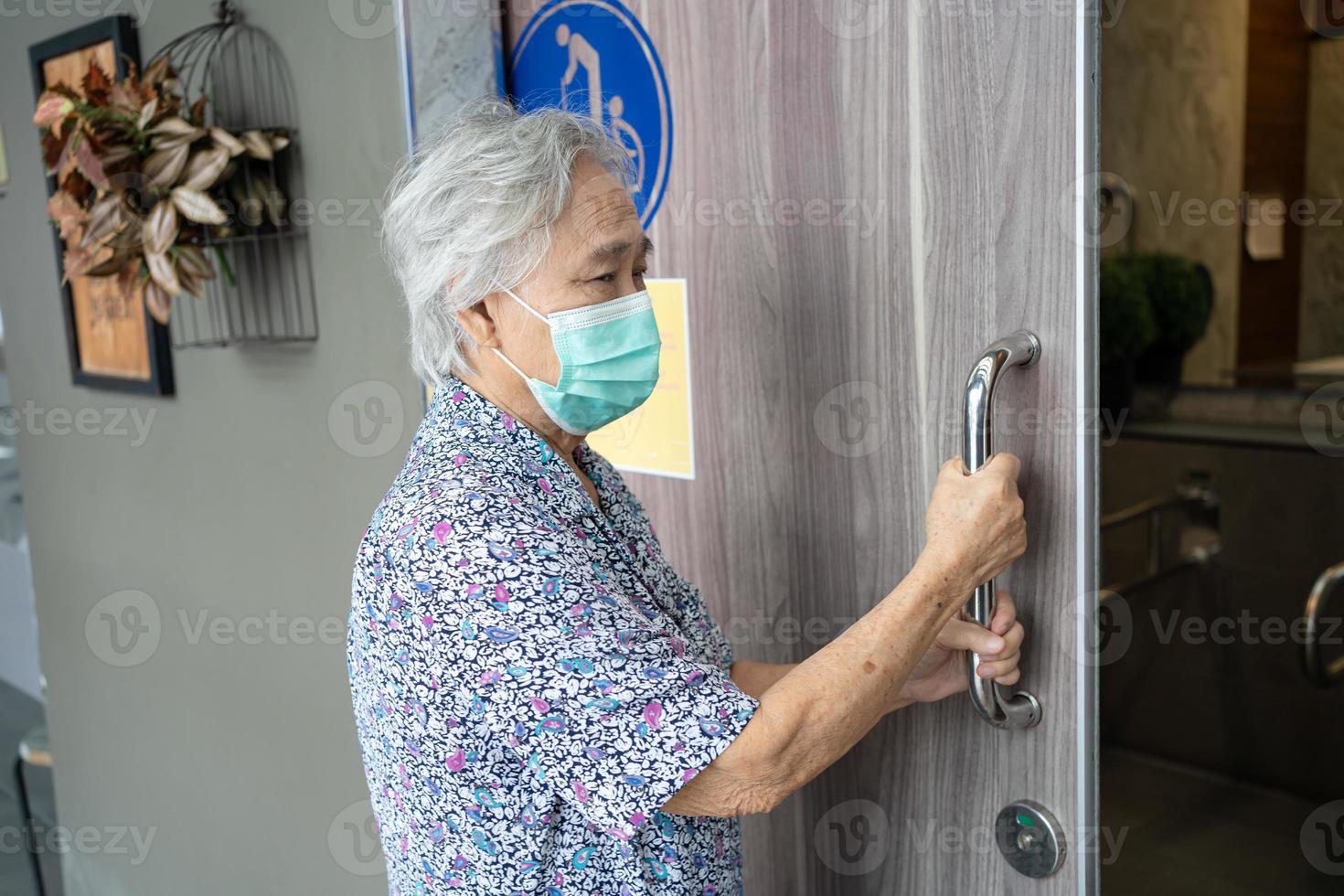 asiatische senior oder ältere alte damenpatientin, die eine gesichtsmaske trägt, öffnet die toilettentür für behinderte menschen zum schutz der sicherheitsinfektion covid-19 coronavirus. foto