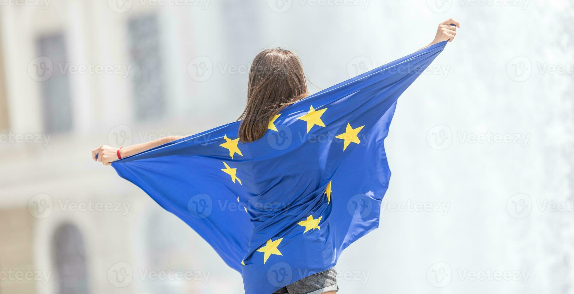 süß glücklich jung Mädchen mit das Flagge von das europäisch Union im Vorderseite von ein historisch Gebäude irgendwo im Europa. foto