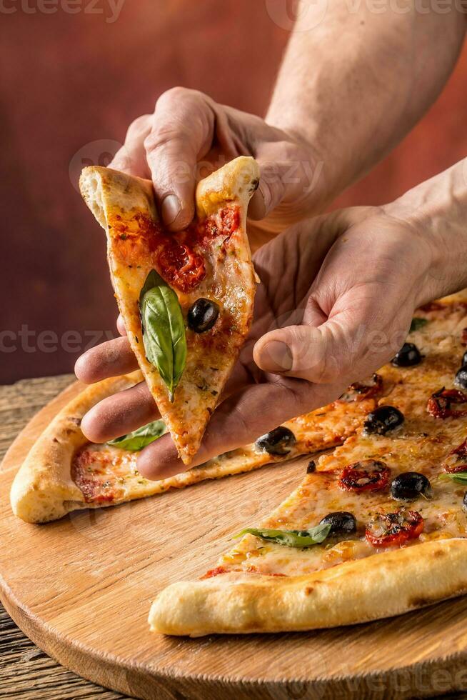 Pizza. lecker frisch Italienisch Pizza serviert auf alt hölzern Tisch. ein Stück von Pizza im ein mans Hand foto