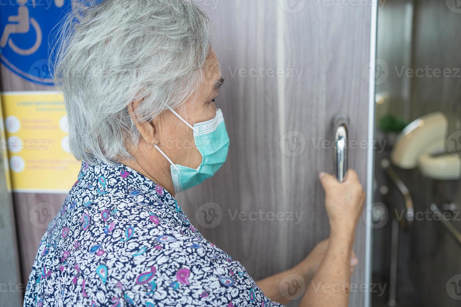 asiatische senior oder ältere alte damenpatientin, die eine gesichtsmaske trägt, öffnet die toilettentür für behinderte menschen zum schutz der sicherheitsinfektion covid-19 coronavirus. foto