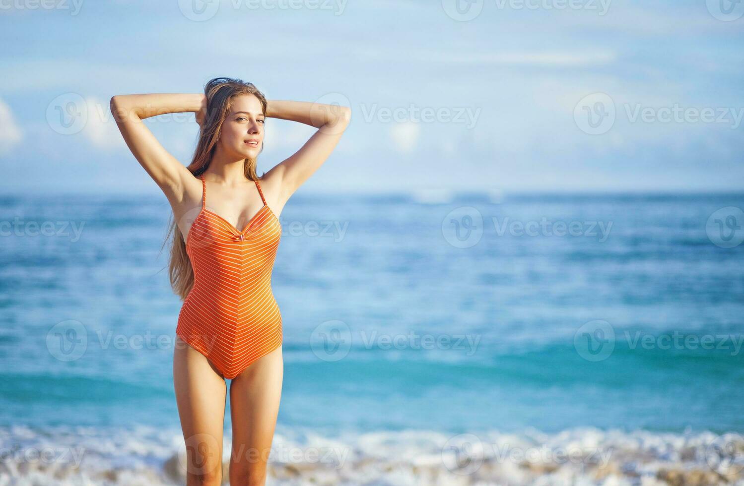 ein Frau im ein Orange Badeanzug Stehen auf das Strand foto