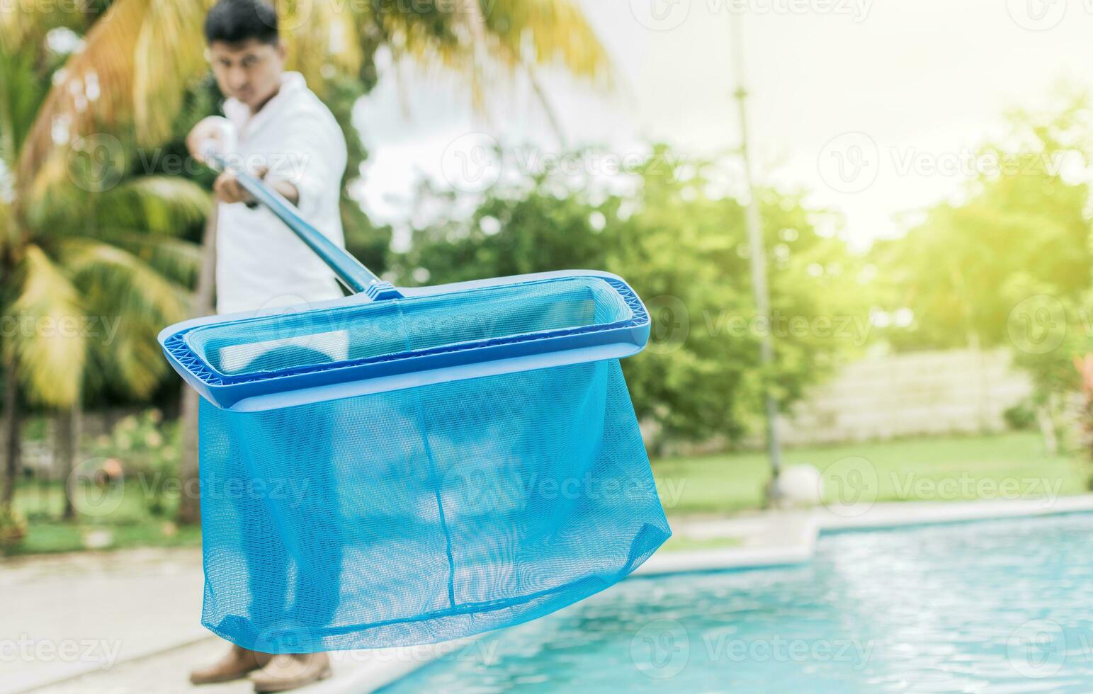 Person mit Skimmer Reinigung Schwimmbad. Mann Reinigung das Schwimmbad mit das Abschäumer, ein Mann Reinigung Schwimmbad mit Blatt Skimmer. Hände halten ein Skimmer mit Blau Schwimmbad im das Hintergrund foto