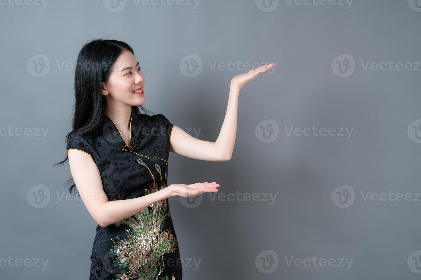 schöne junge asiatische frau trägt chinesisches traditionelles kleid mit der hand, die auf der seite präsentiert foto