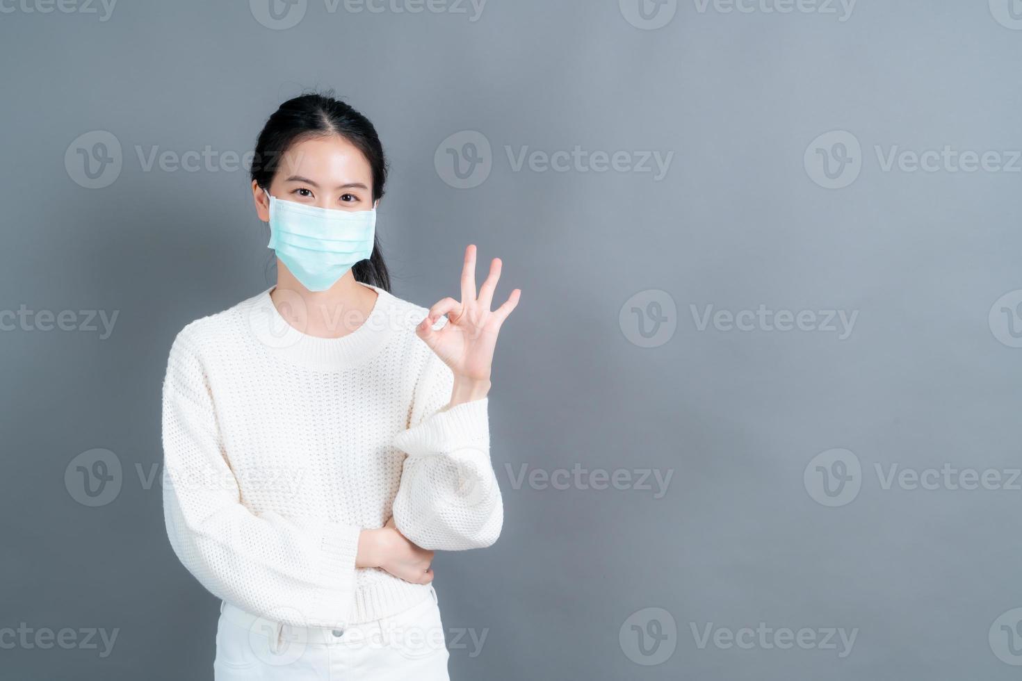 junge asiatische frau, die eine medizinische gesichtsmaske trägt und ein ok-zeichen zeigt foto